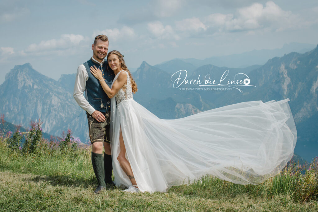 Hochzeitspaar in Tracht am Berg, Bräutigam steht neben Braut auf einer Wiese