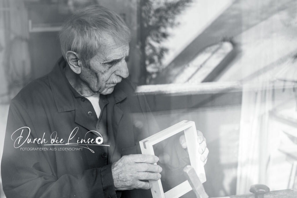 Projekt Forever Active - ein Tischler aus Leidenschaft, durch das Fenster fotografiert mit einem Holzstück in der Hand