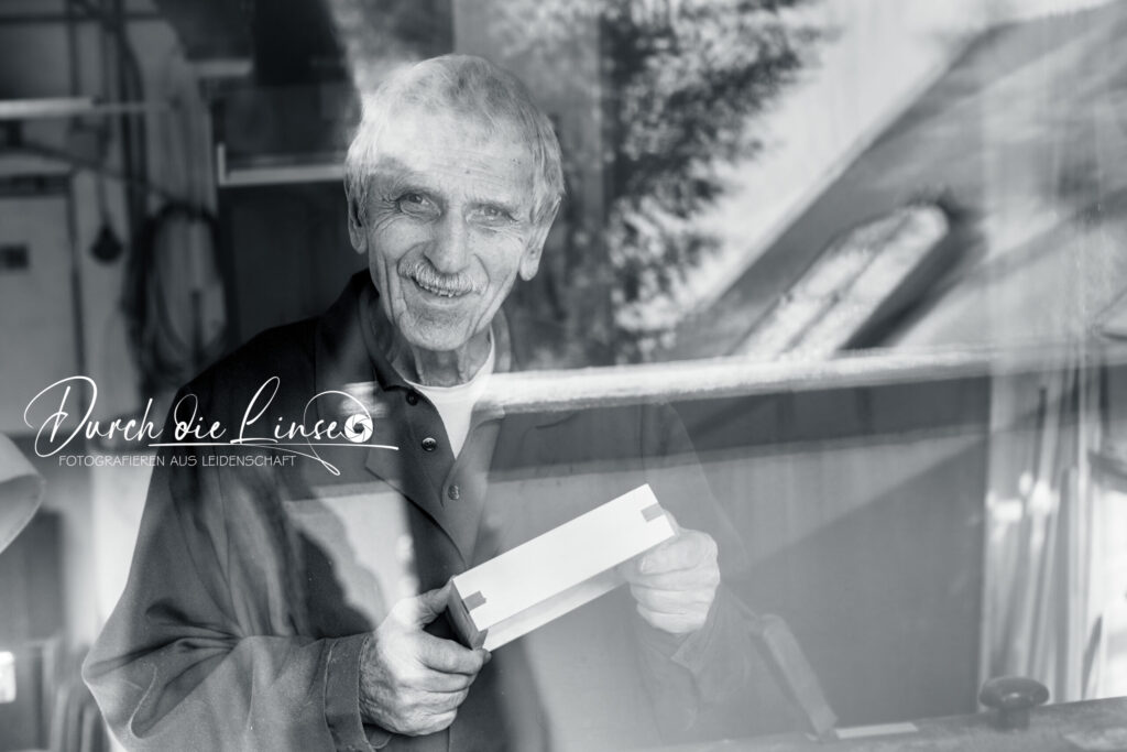 Projekt Forever Active - ein Tischler aus Leidenschaft, durch das Fenster fotografiert mit einem Holzstück in der Hand