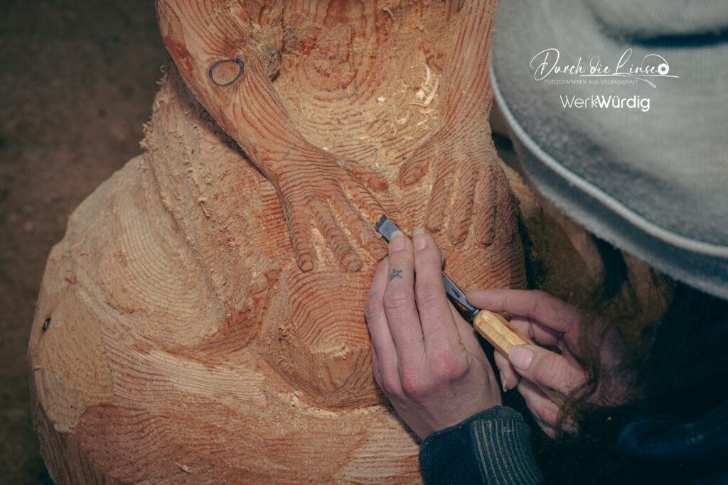Holzkünstlerin Lisa Hirschbichler arbeitet mit einem Werkzeug an den Händen einer Holzskulptur.