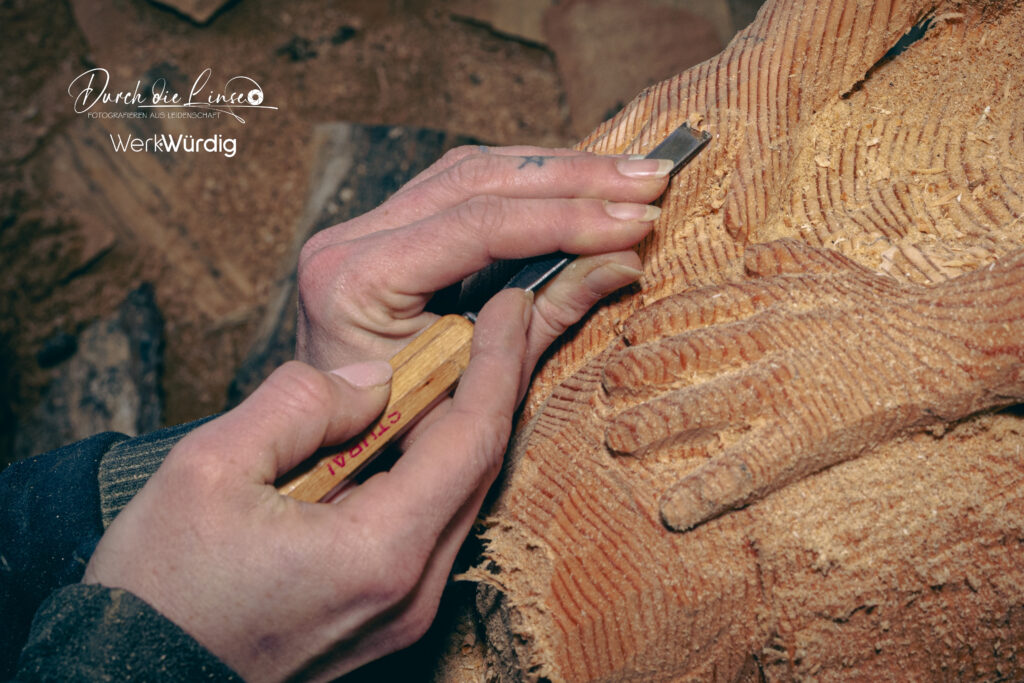 Holzkünstlerin Lisa Hirschbichler arbeitet mit einem Werkzeug an den Händen einer Holzskulptur.