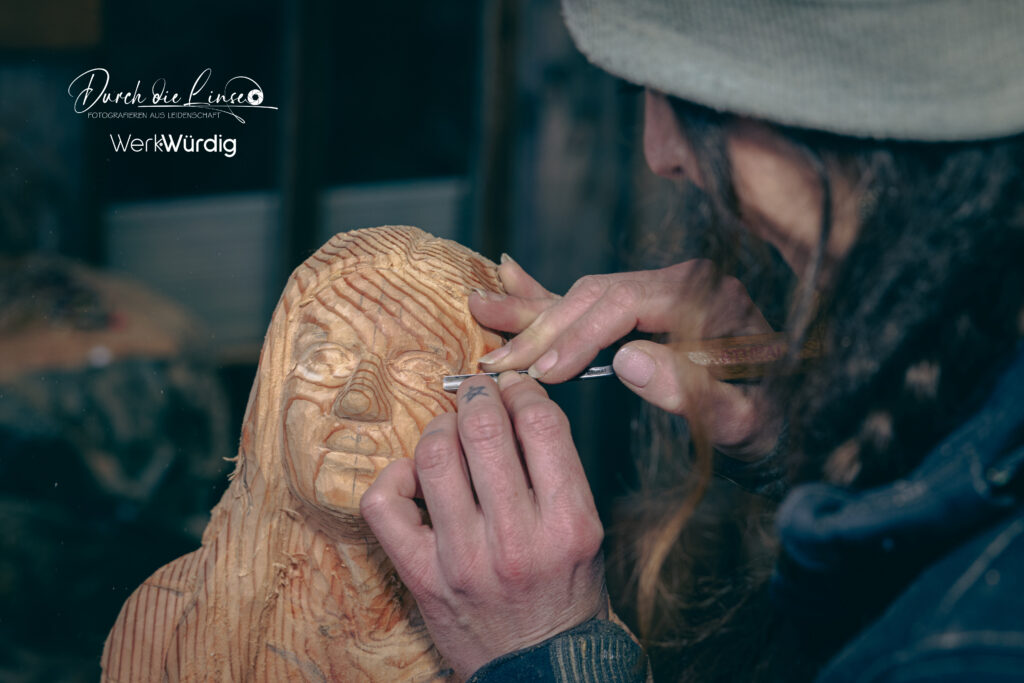 Holzkünstlerin Lisa Hirschbichler arbeitet mit einem Werkzeug an den Augen einer Holzskulptur.